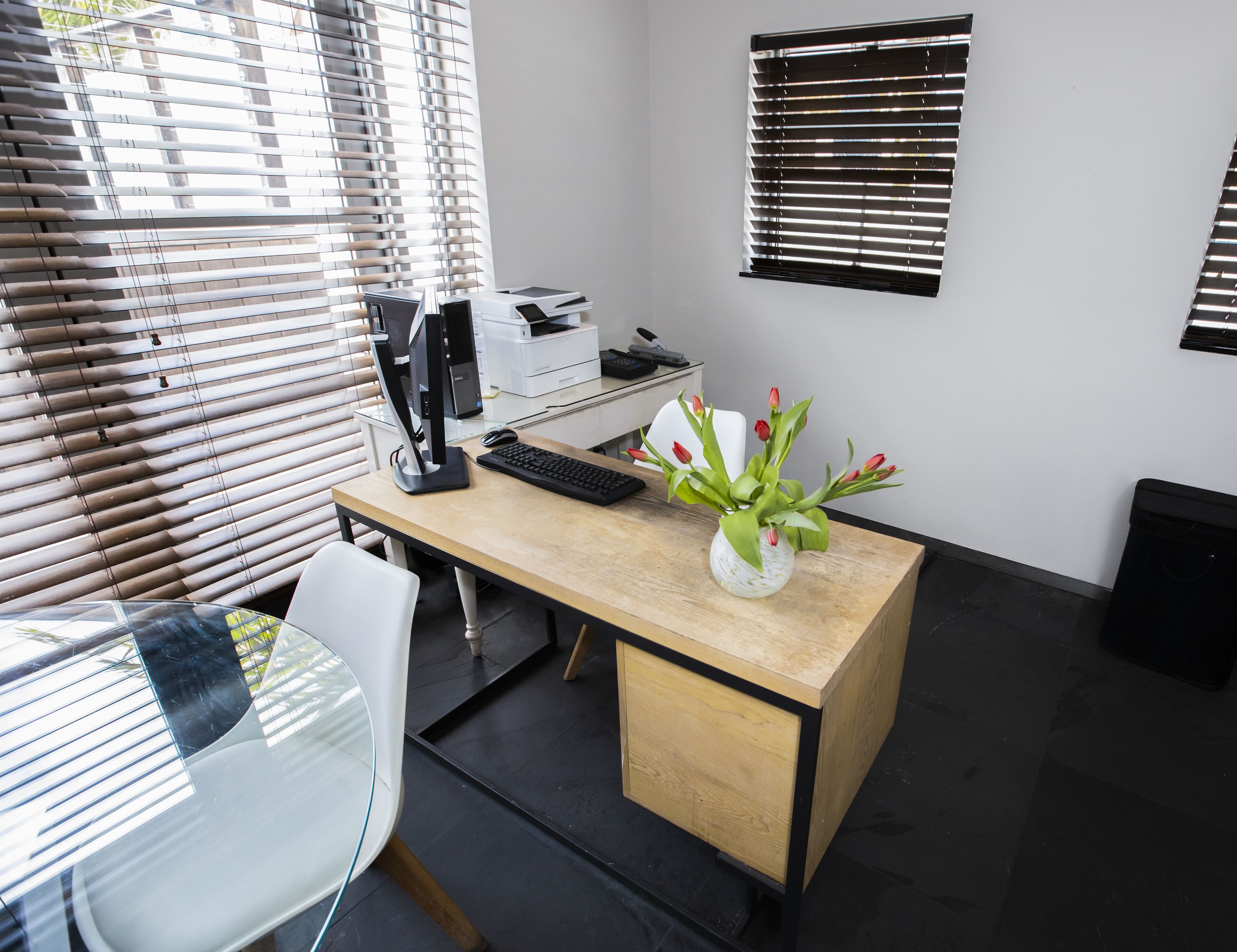 A modern office space with a wooden desk, computer, printer, and a vase with flowers.