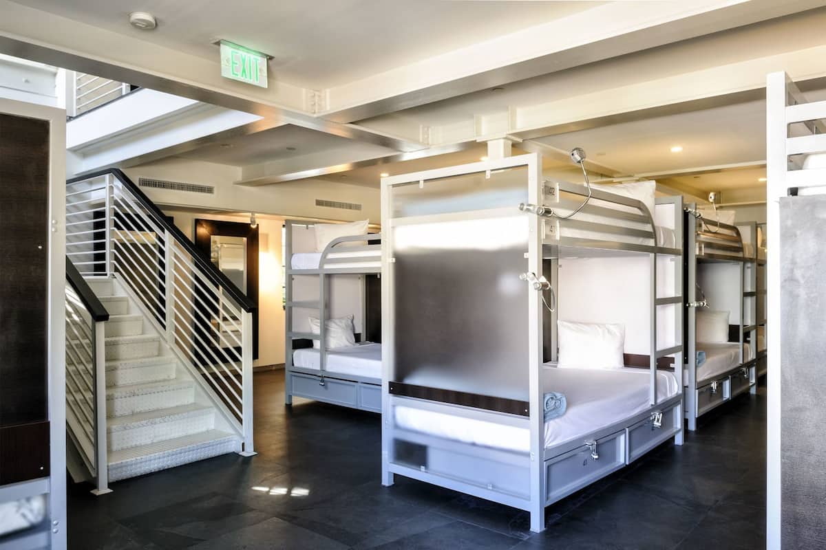 A modern hotel room with bunk beds, a staircase, and an exit sign.