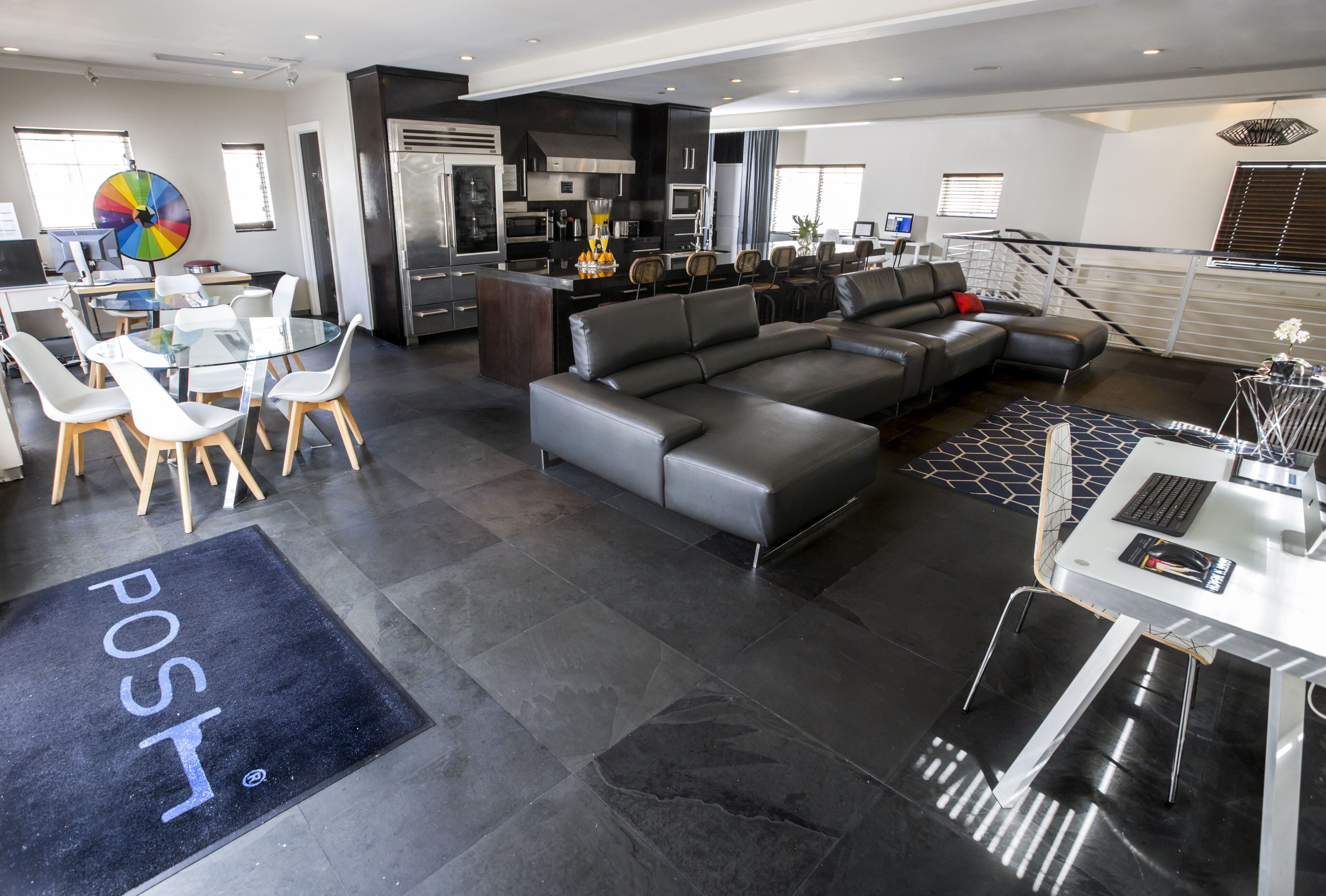 A modern living room with a sectional sofa, a glass dining table, and a kitchen area with stainless steel appliances.