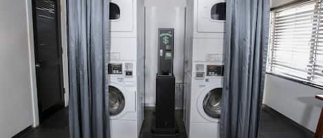 A laundry facility with two front-loading washing machines, a control panel, and grey curtains.