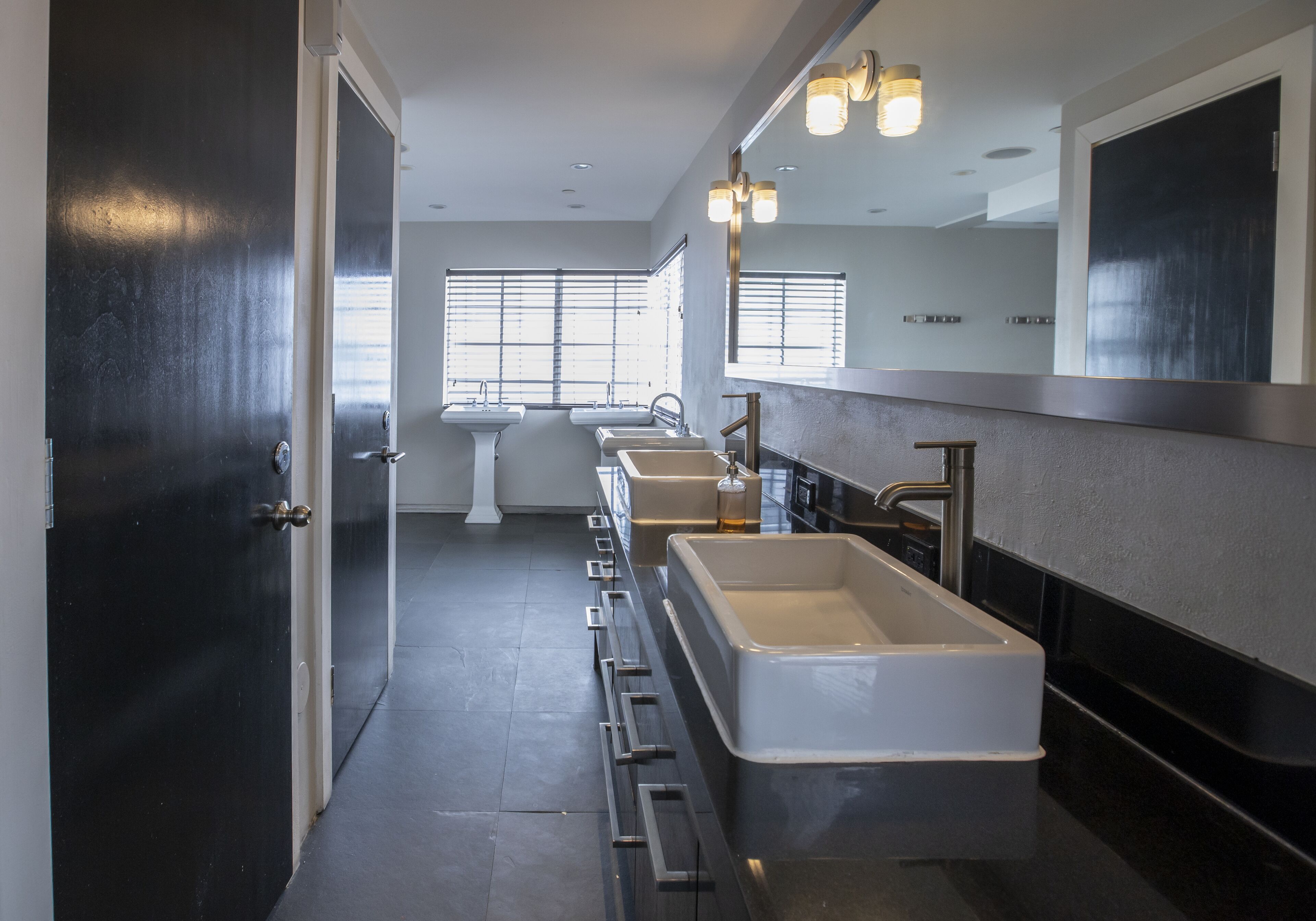 Un bagno moderno con un lungo mobile lavabo, diversi lavabi e uno specchio grande.