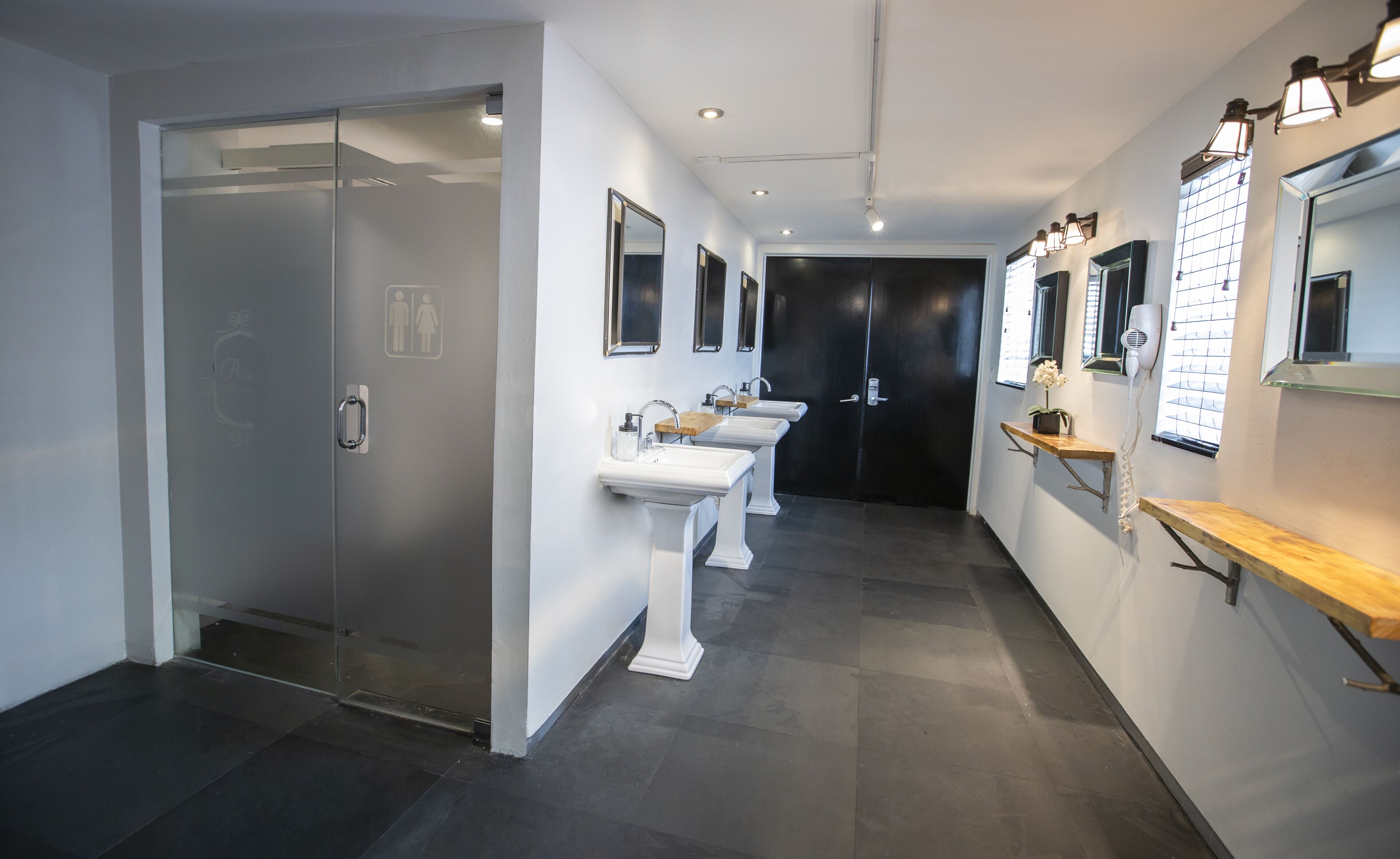 A modern bathroom with three sinks, a glass door, and a black door.