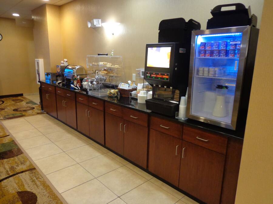 Uma área de recepção de hotel com máquina de café, refrigerador e dispensador de bebidas para autoatendimento.