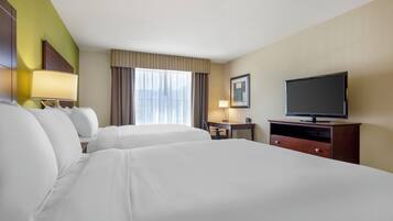 Una habitación de hotel con dos camas, un televisor, un escritorio con lámpara y una ventana con cortinas.