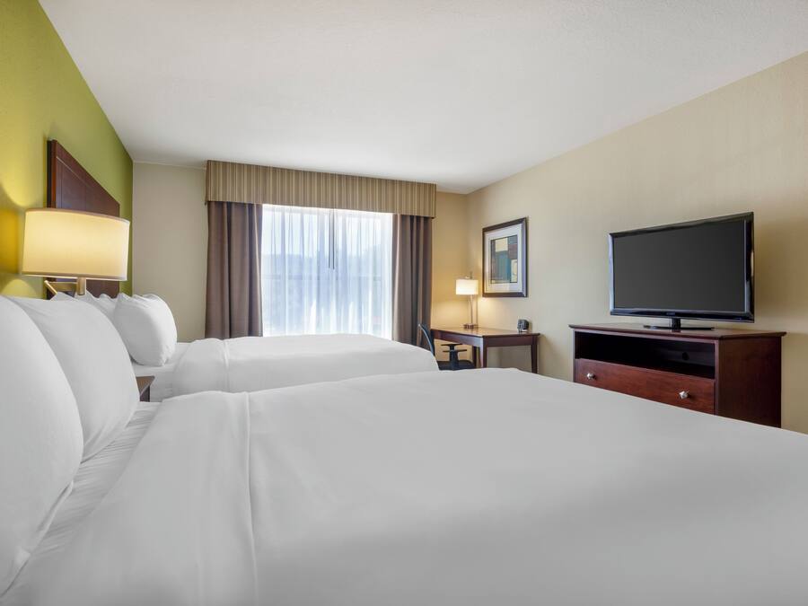 Una habitación de hotel con dos camas, un televisor, un escritorio con lámpara y una ventana con cortinas.