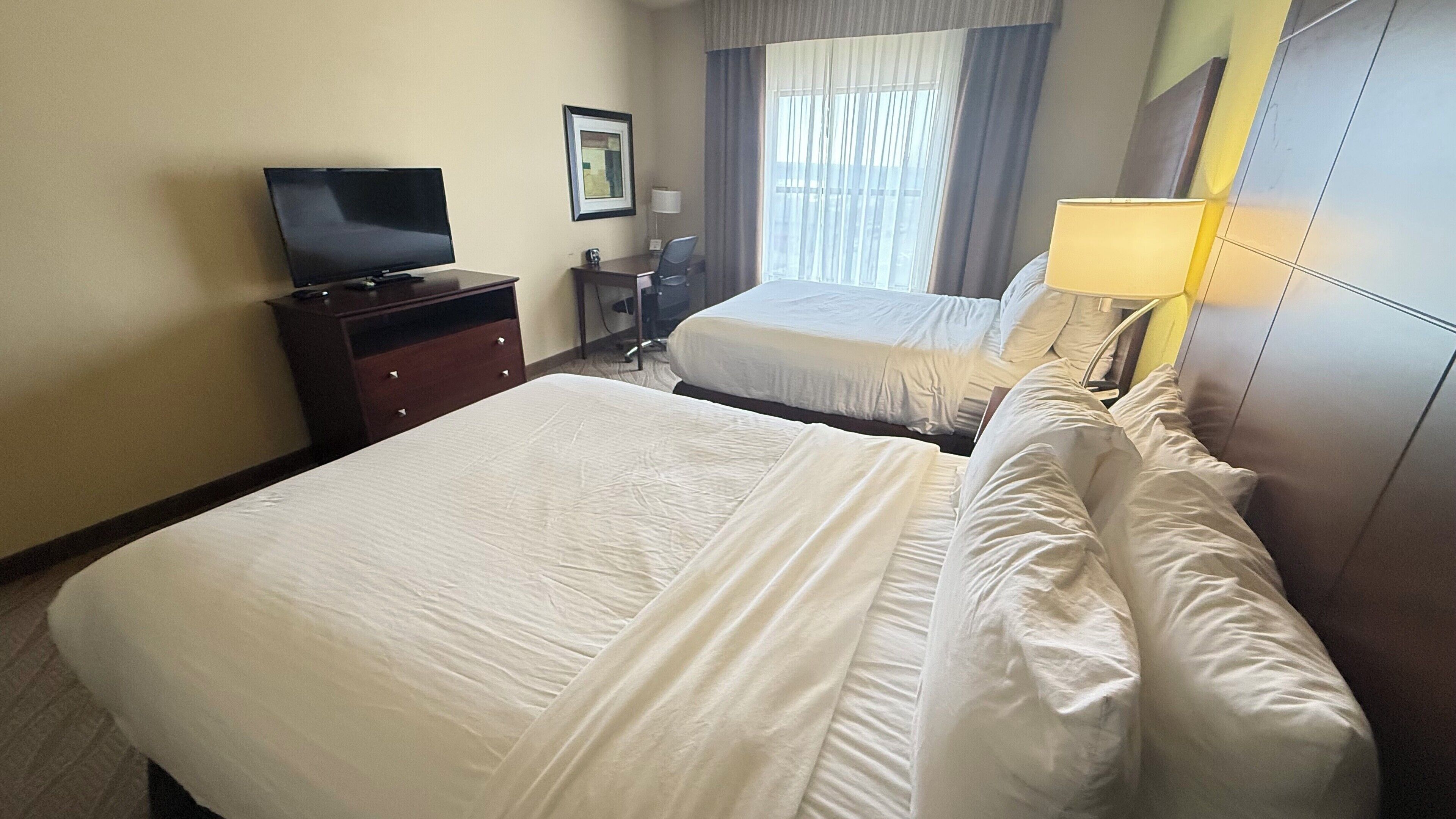 A hotel room with two beds, a TV, a desk, and a window with curtains.