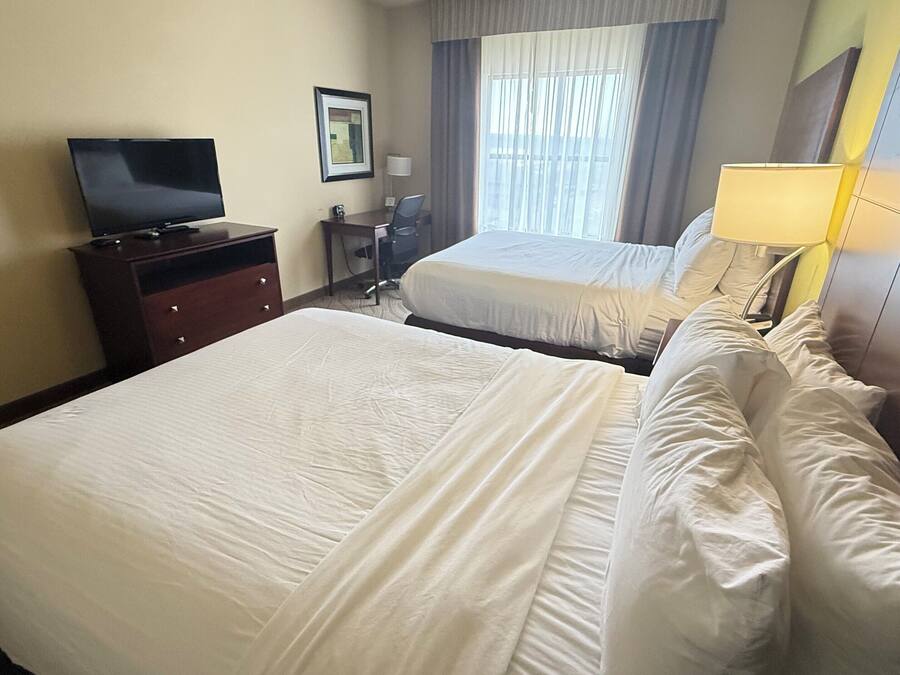A hotel room with two beds, a TV, a desk, and a window with curtains.