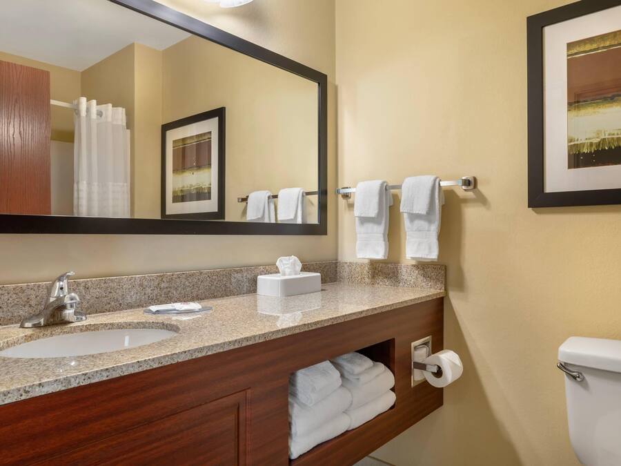 A bathroom with a granite countertop sink, a mirror, a towel rack, a toilet, and a framed picture on the wall.