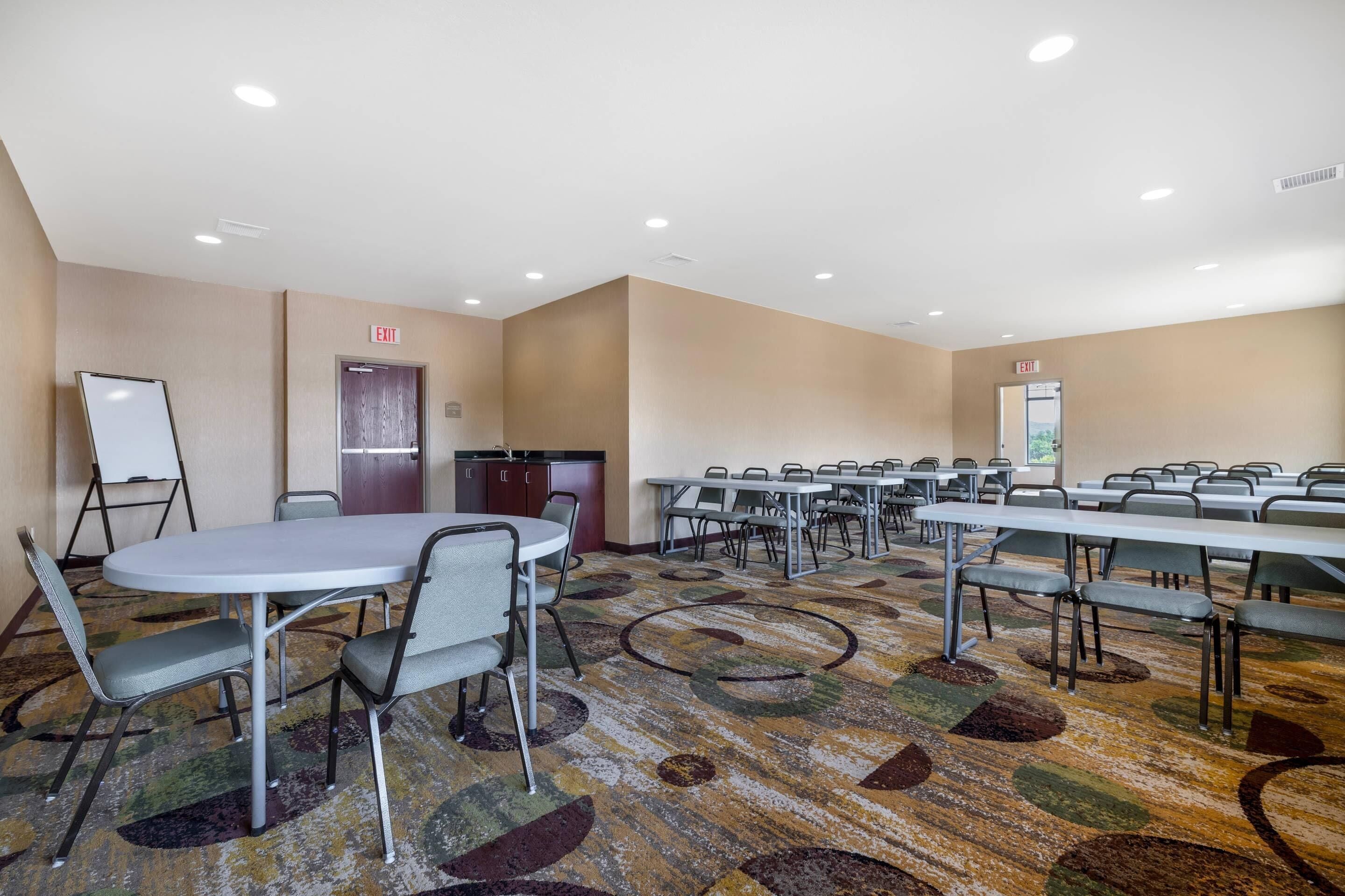 A conference room with multiple tables and chairs, a whiteboard, and an exit sign.