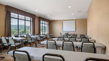 A conference room with multiple tables and chairs, large windows with blinds, and a projection screen on the wall.
