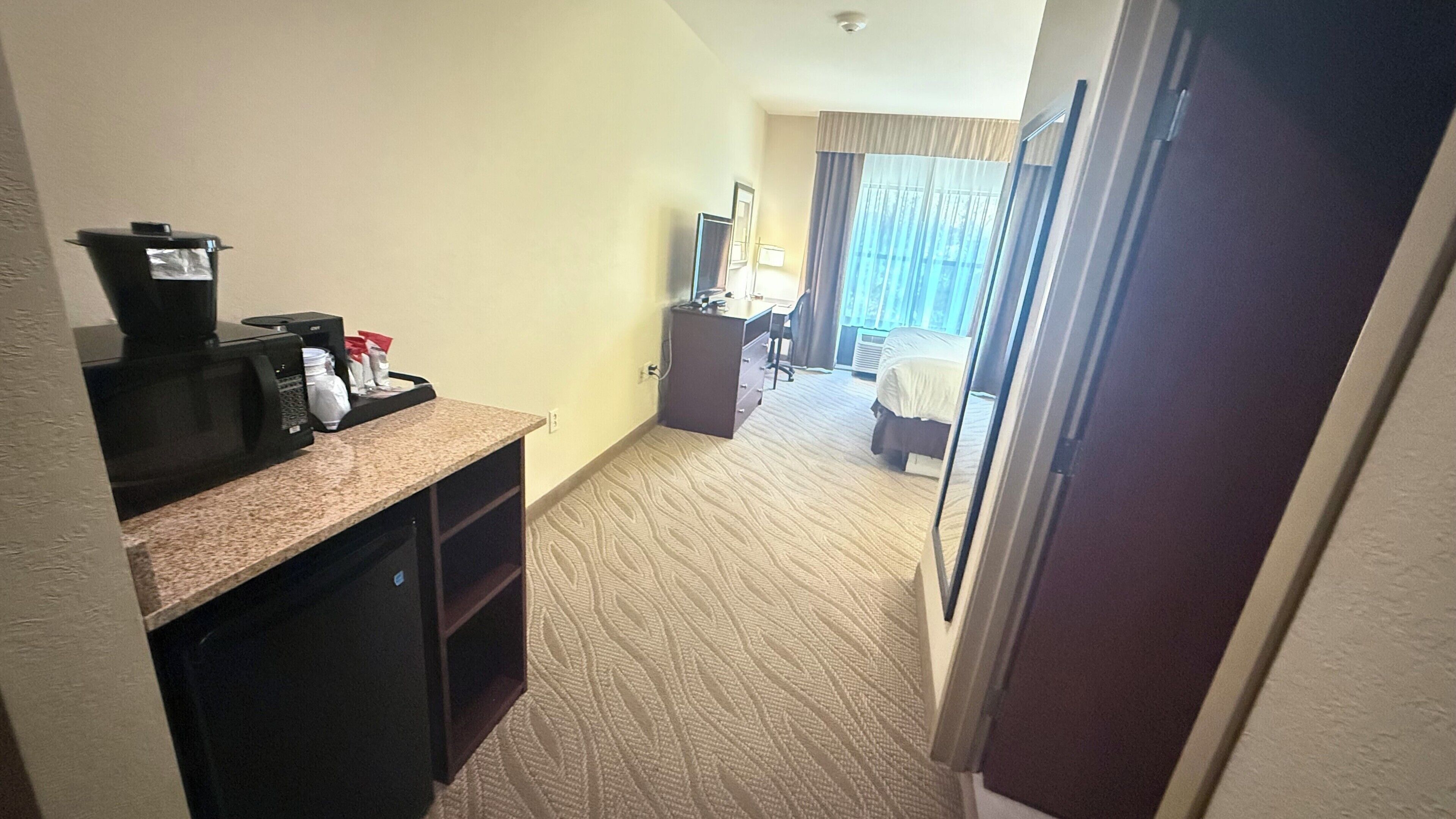 Een hotelkamer met een kitchenette, een bed, een bureau en een badkamer.