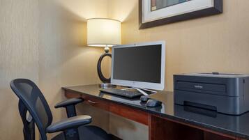 A hotel room desk with a desktop computer, a printer, a chair, and a lamp.