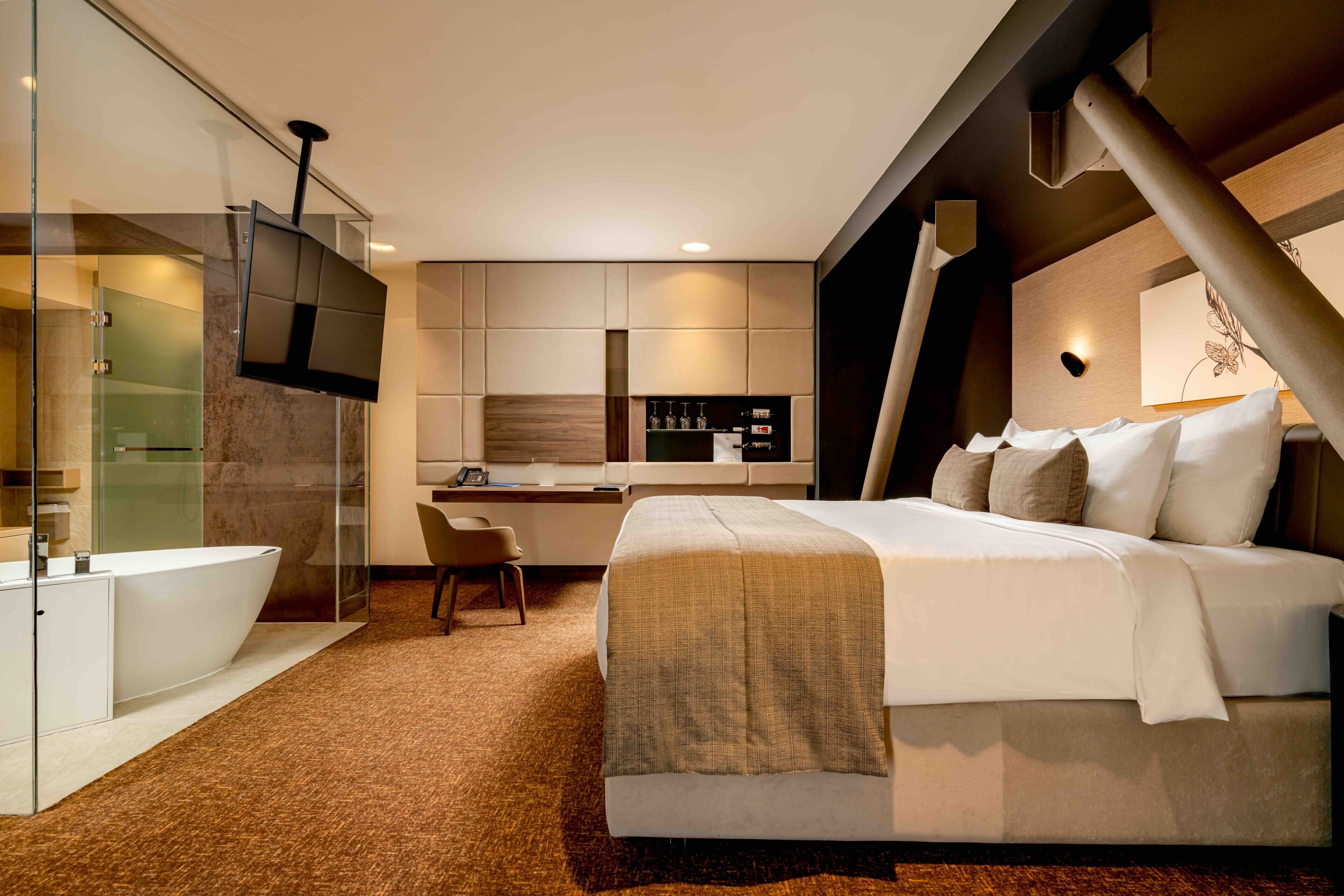 A modern hotel room with a large bed, a separate bathroom, a small desk, and a TV mounted on the wall.