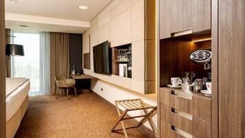 A hotel room with a bed, a desk, a chair, a TV, a minibar, and a window with curtains.