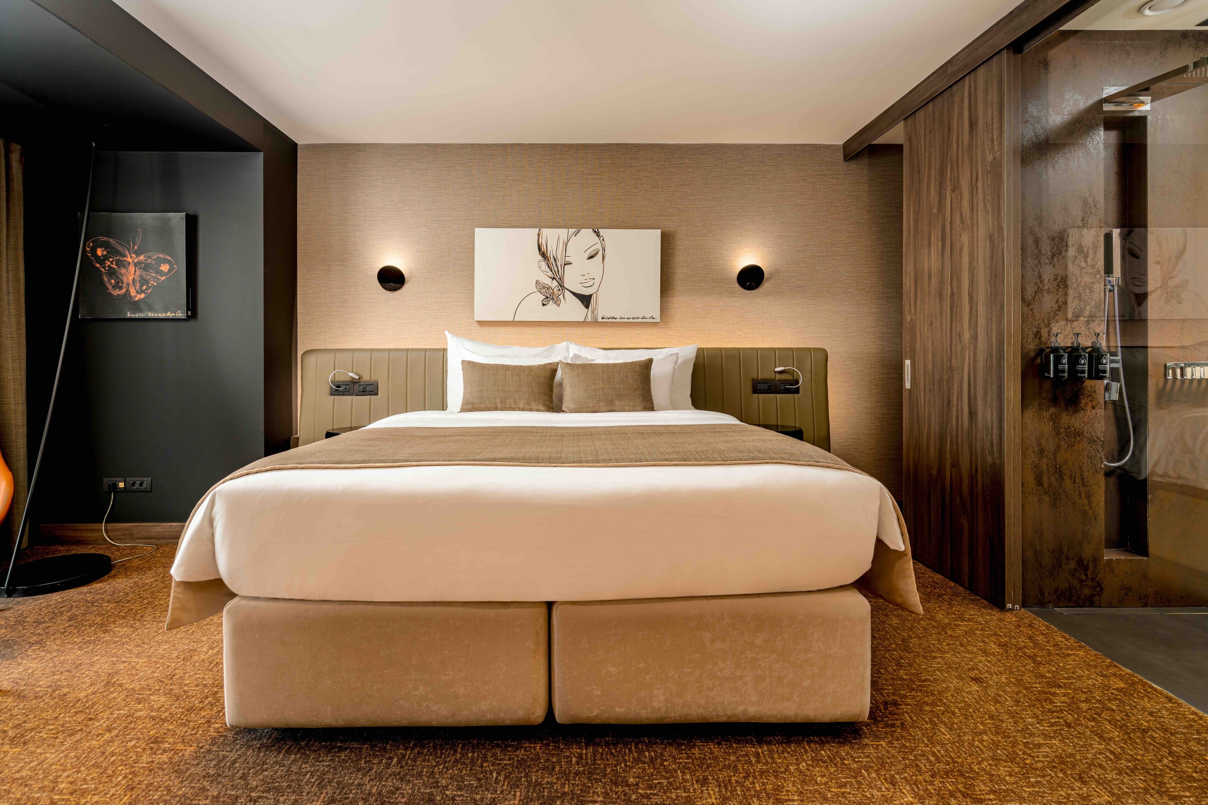 Ein modernes Hotelzimmer mit einem großen Bett, einem Holzkopfstück, einem an der Wand befestigten Kunstwerk und einer integrierten Dusche.