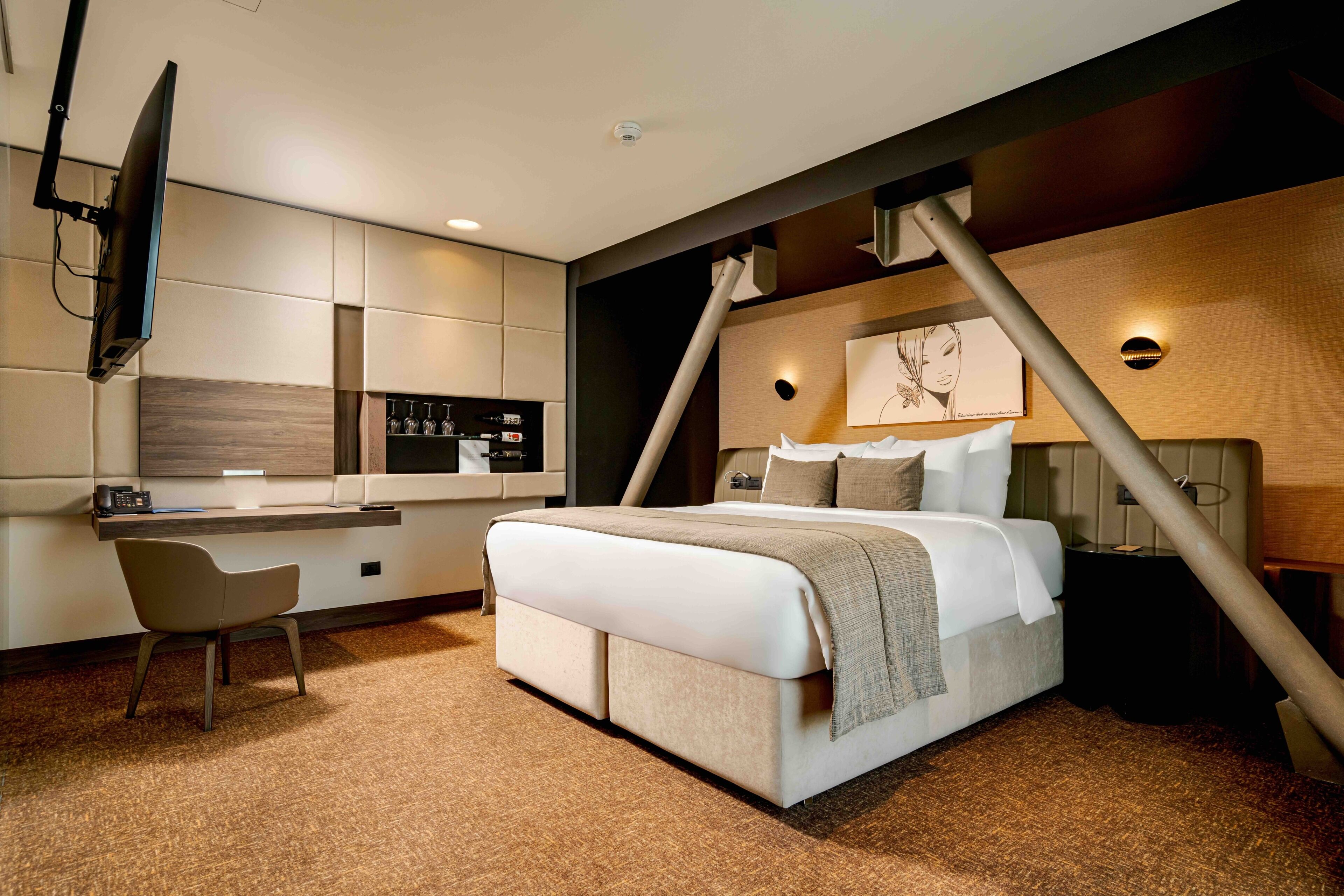 Una habitación de hotel moderna con cama, escritorio, silla, televisor y una obra de arte colgada en la pared.