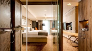 A modern hotel room with a glass partition, a bed, a desk, and a kitchenette. - Kronwell Brasov Hotel (Brasov)