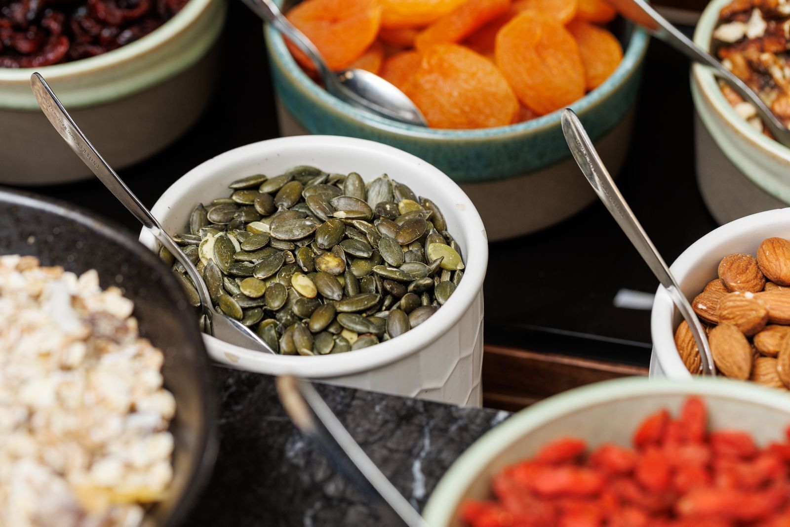 Variedad de alimentos en cuencos, como semillas de calabaza, almendras y frutas secas.