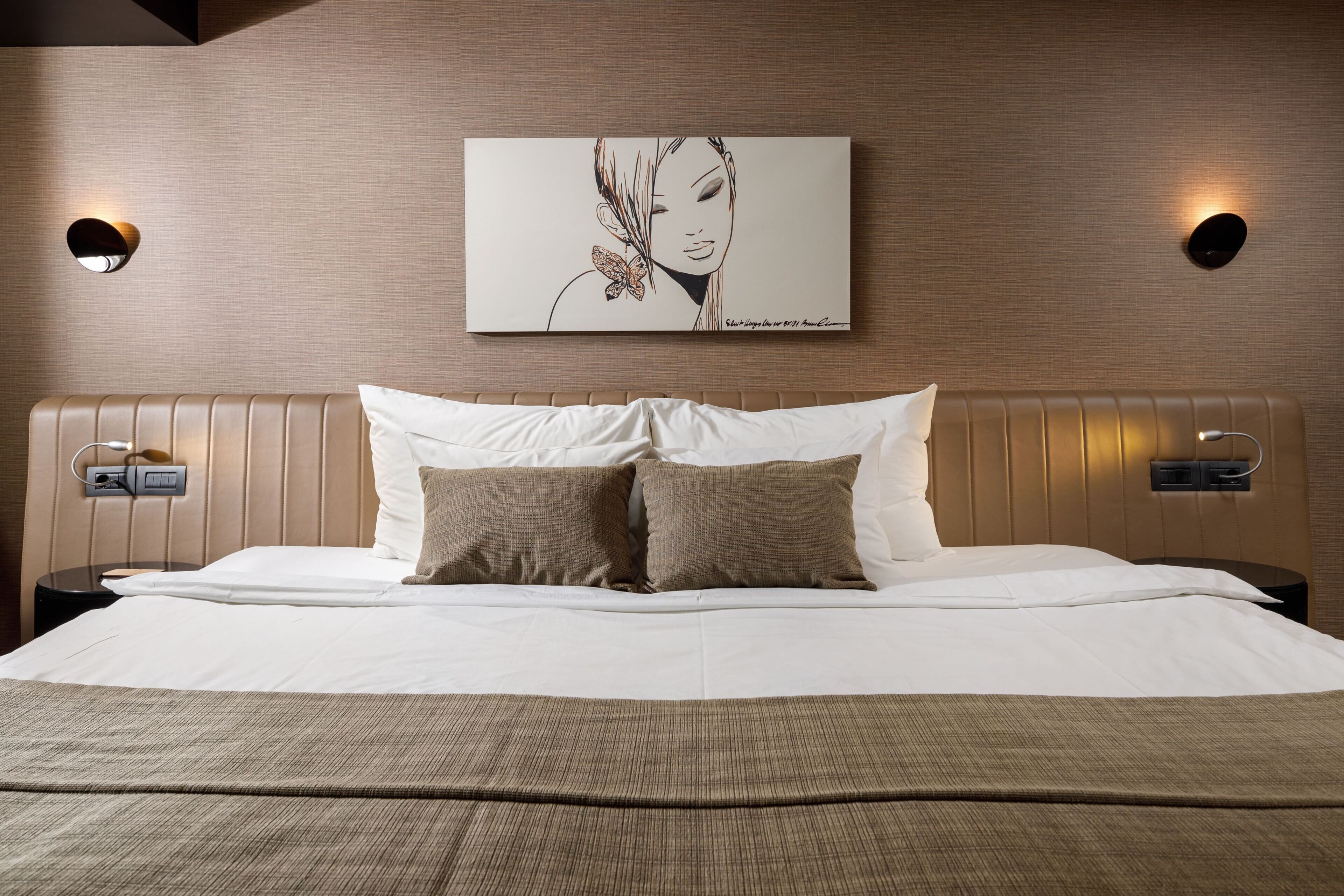 A hotel room with a large bed, two bedside tables, a wall-mounted artwork, and a textured wall.