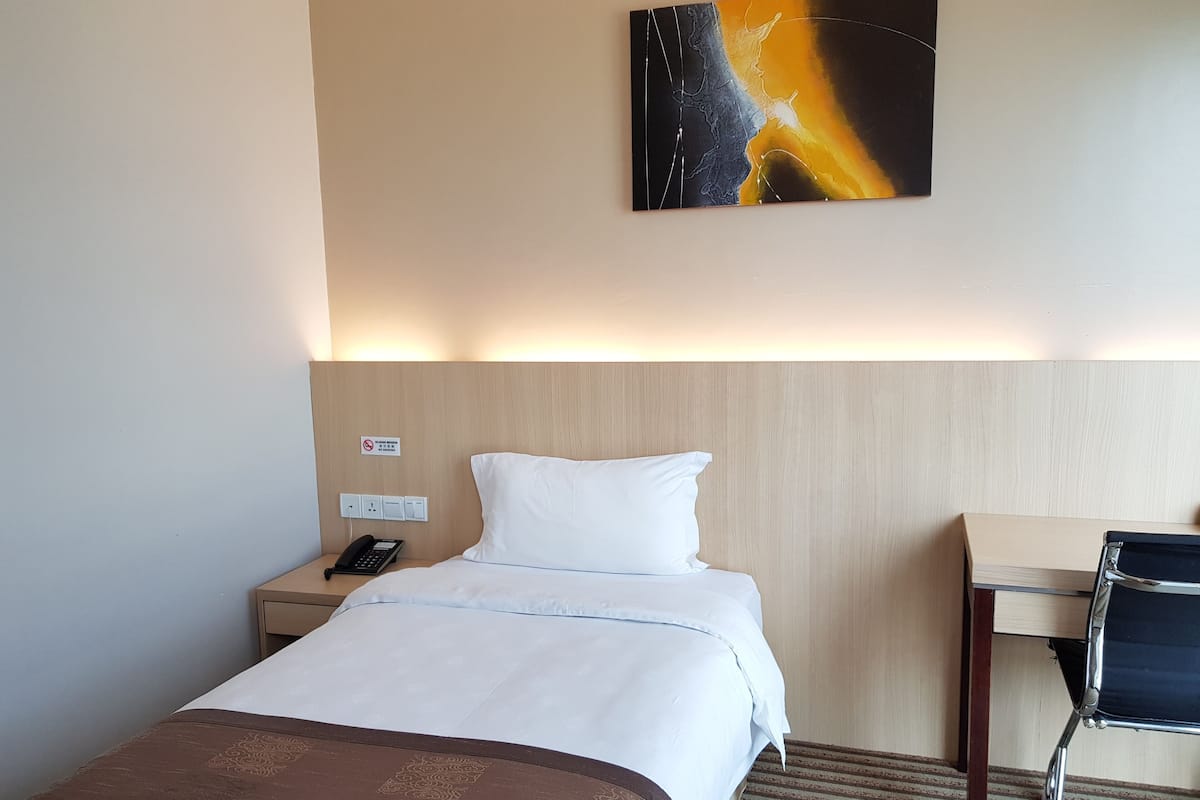 Hotellihuone, jossa on sänky, yöpöytä ja työpöytä tuolilla.