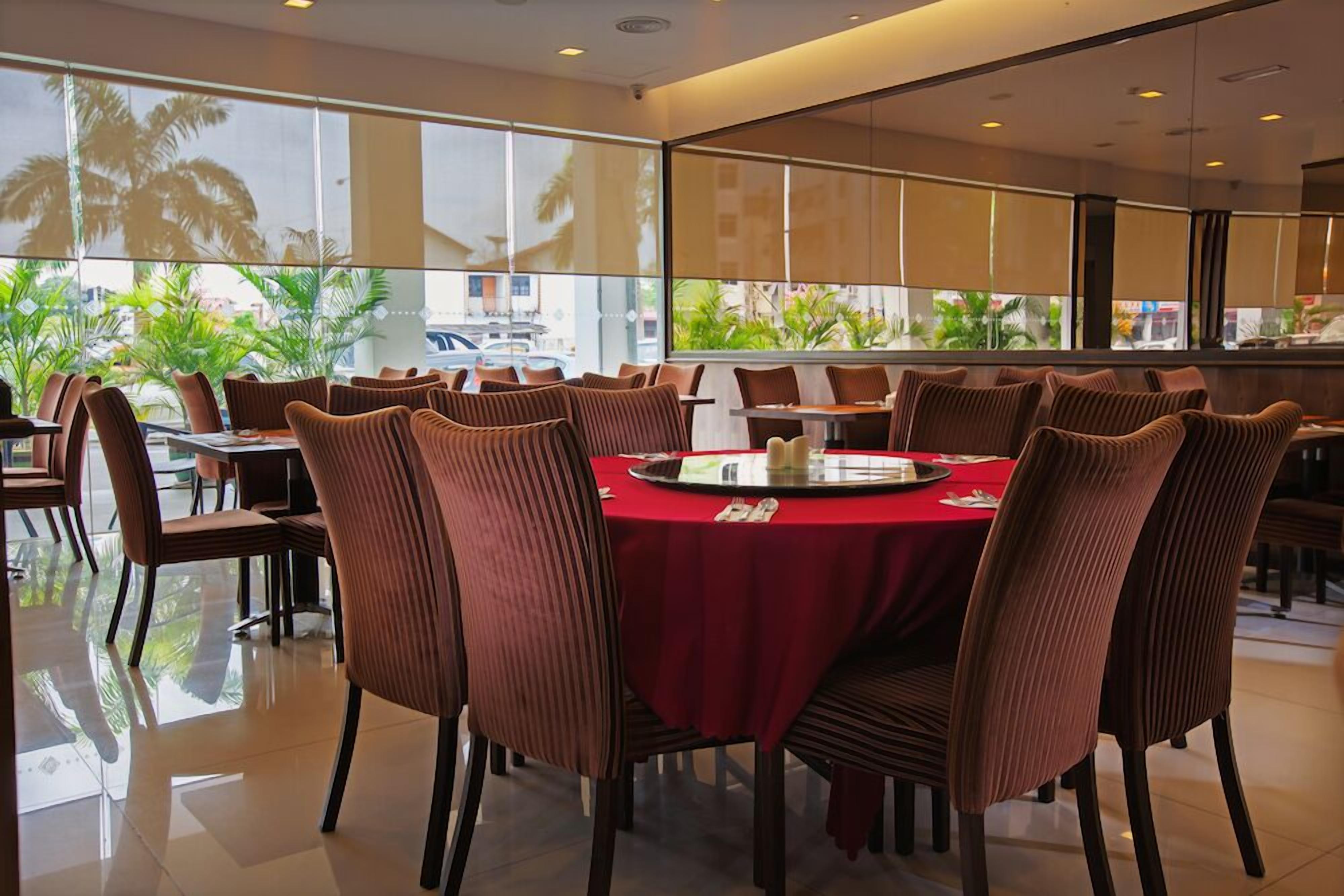 A modern dining area with round tables and brown upholstered chairs, large windows with a view of palm trees and buildings.