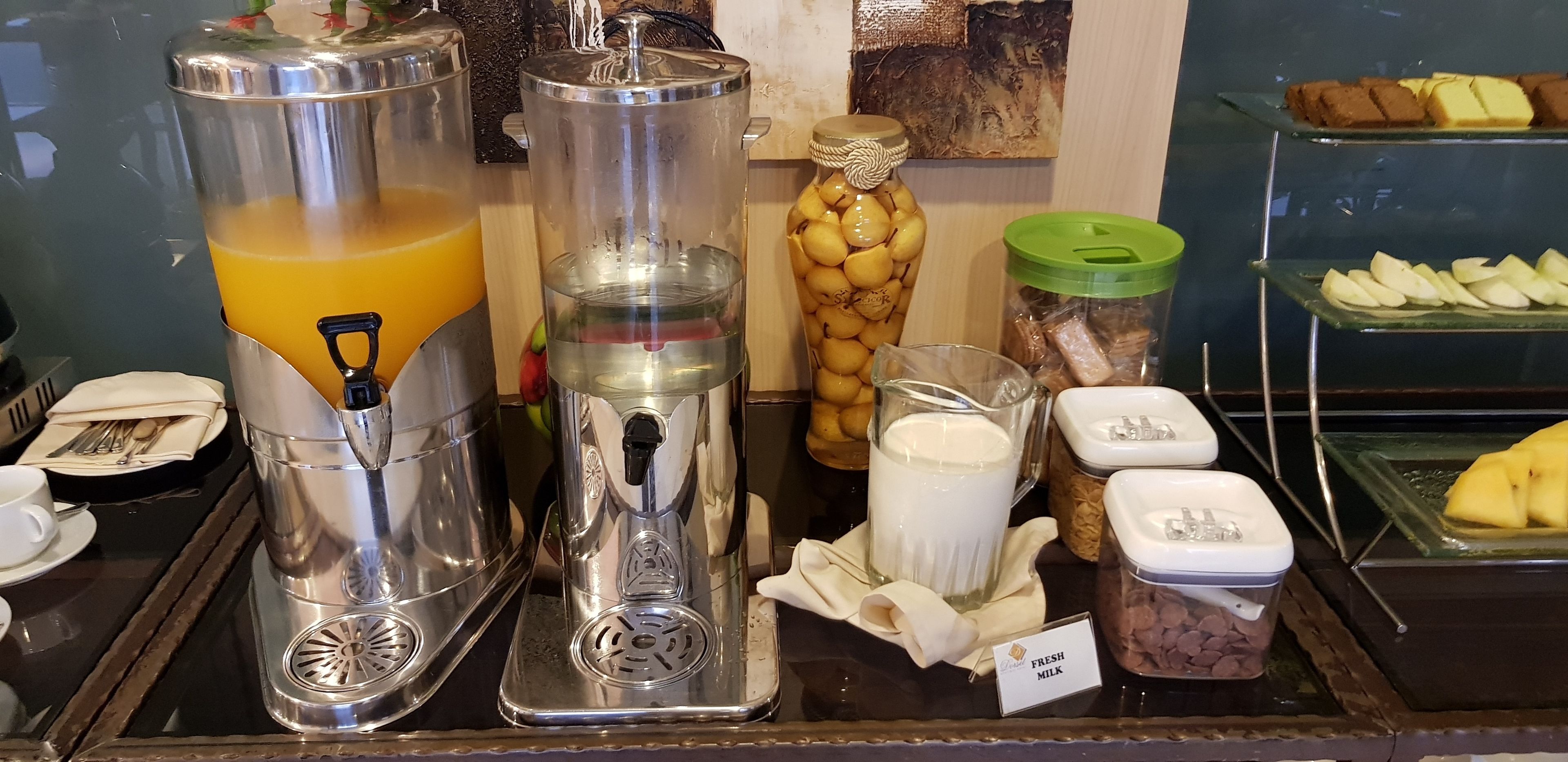 A breakfast bar with a juice dispenser, a milk dispenser, and various food items including fresh milk, preserved lemons, and snacks.