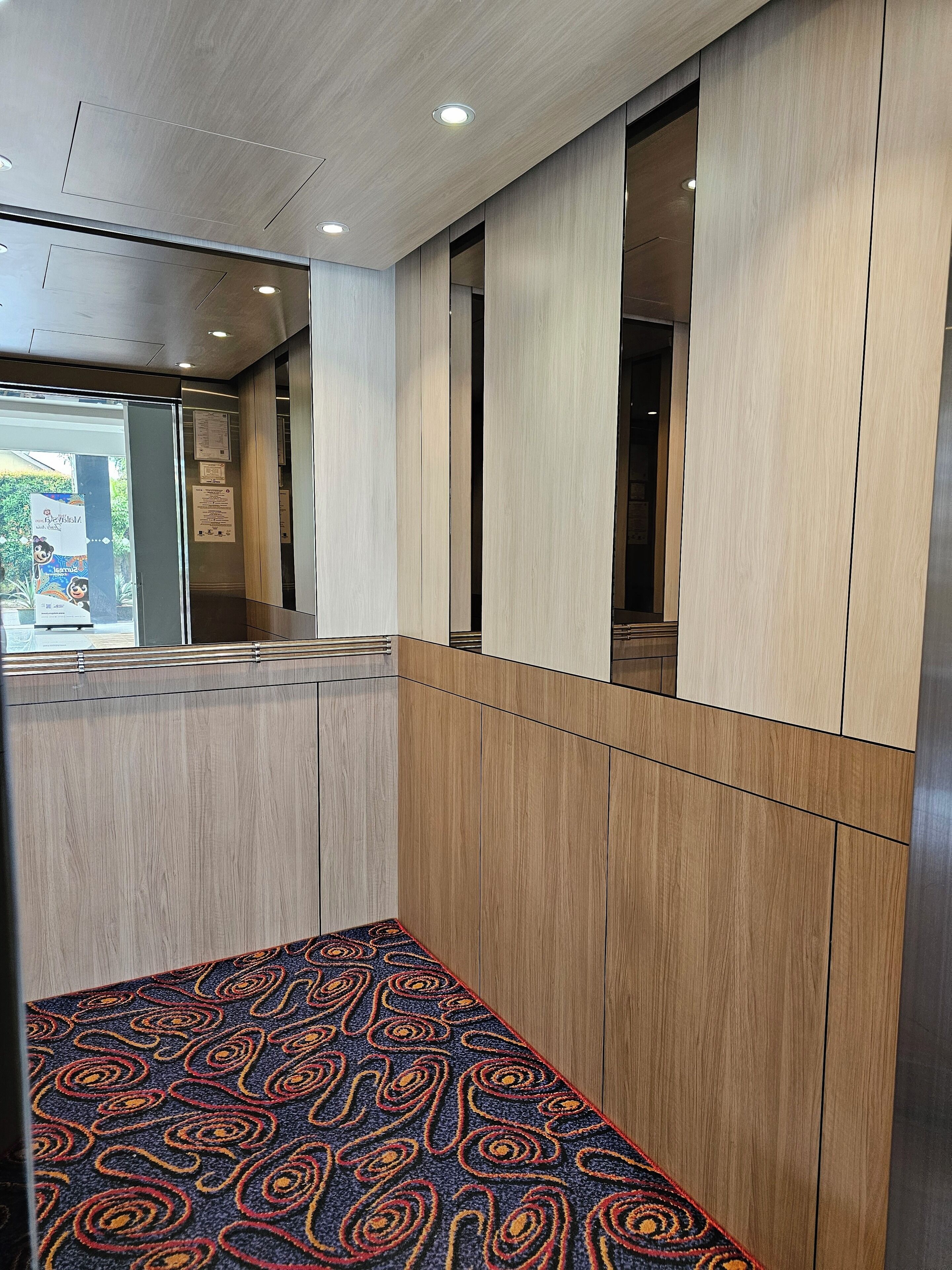 Un hall d’hôtel avec un tapis à motifs, des lambris en bois et une porte vitrée donnant sur l’extérieur.