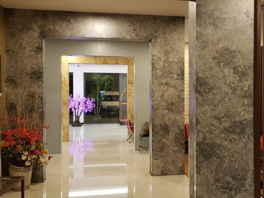 A hallway with a marble wall, a glass door leading to a room, and a potted plant with flowers.