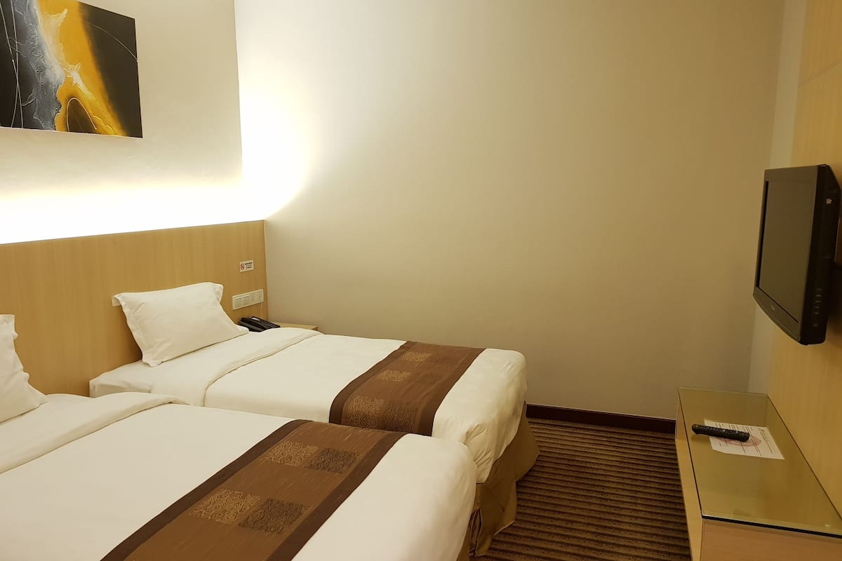 Hotellihuone, jossa on kaksi sänkyä, taulutelevisio, yöpöytä ja taulu seinällä.