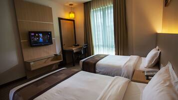 Een hotelkamer met twee bedden, een bureau, een televisie en een groot raam met gordijnen.
