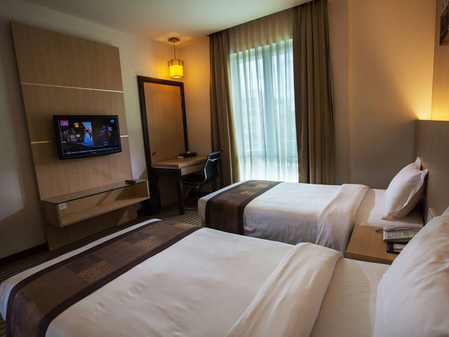 Een hotelkamer met twee bedden, een bureau, een televisie en een groot raam met gordijnen.