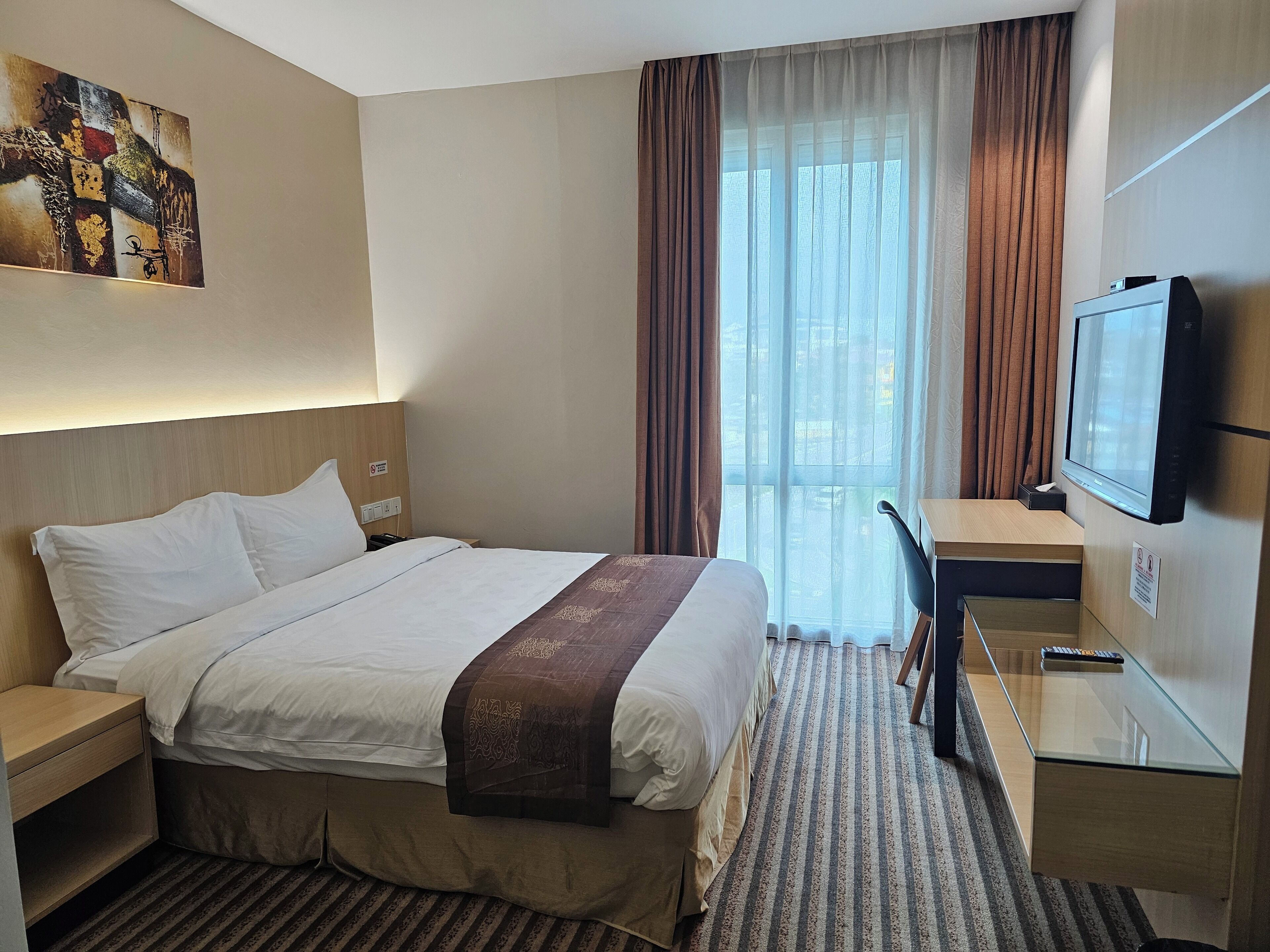 Une chambre d’hôtel avec un lit, un bureau, une télévision et une fenêtre avec des rideaux.