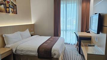Une chambre d’hôtel avec un lit, un bureau, une télévision et une fenêtre avec des rideaux.