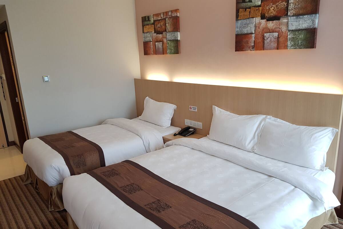 Hotellihuoneessa on kaksi sänkyä, joissa on valkoiset lakanat ja ruskeat koristereunat. Huoneessa on seinään kiinnitetty puhelin ja valokatkaisin.