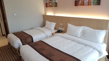 A hotel room with two beds, each with white linens and brown decorative borders. There is a wall-mounted phone and a light switch.