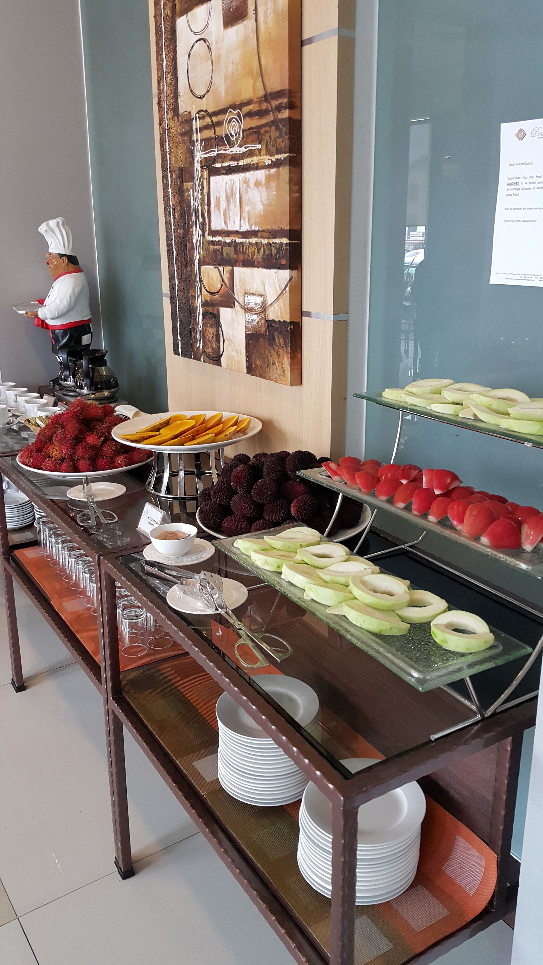 A buffet with various fruits and a chef statue.