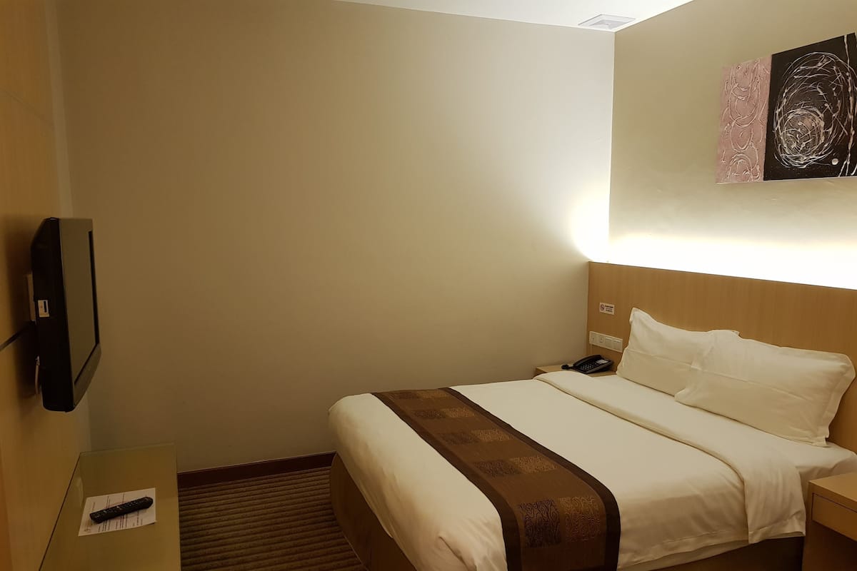Hotellihuone, jossa on sänky, yöpöytä ja seinälle asennettu televisio.