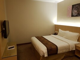 Una habitación de hotel con cama, mesita de noche y televisor montado en la pared.