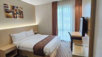 A hotel room with a large bed, a bedside table, a TV, and a window with curtains.