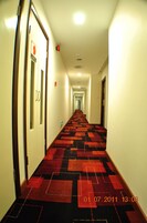 Un pasillo de hotel con alfombra de diseño rojo y negro, paredes blancas y puertas con el cartel 'DD'.
