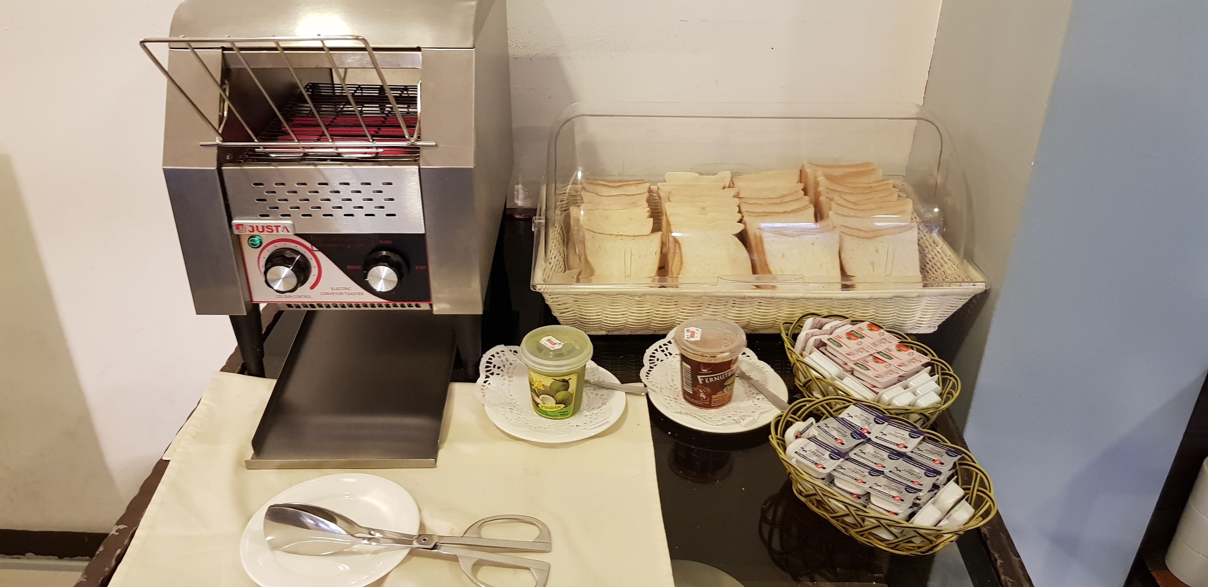 A breakfast setup with a toaster, bread, butter, jam, and condiments.