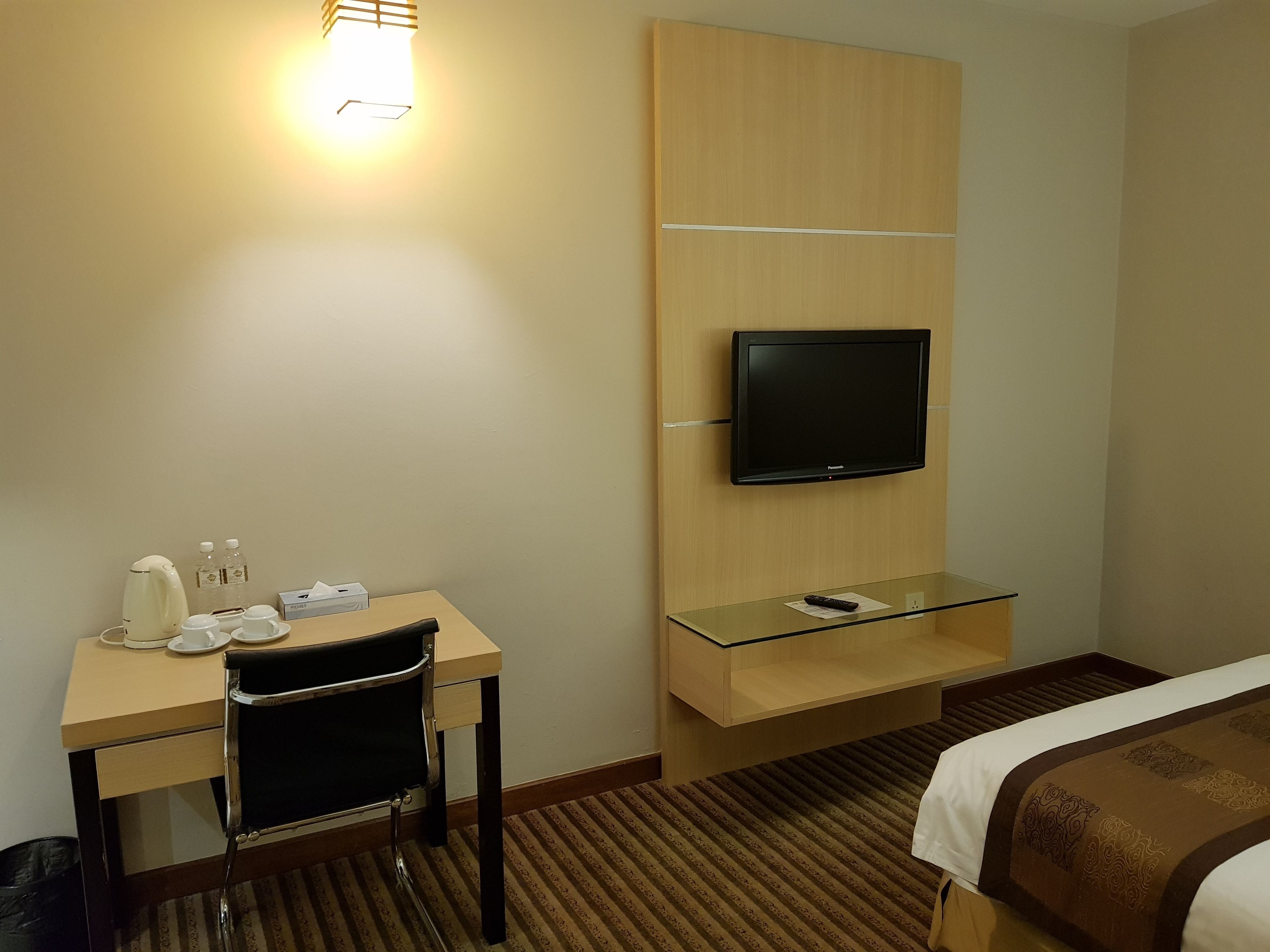 Hotelkamer met een bed, een bureau met stoel, een aan de muur bevestigde televisie en een klein plankje eronder.