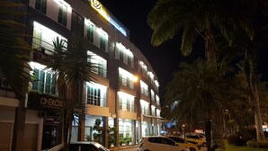A multi-story hotel with illuminated signage, parked cars, and palm trees. - DeHome Boutique Hotel (Kuching)