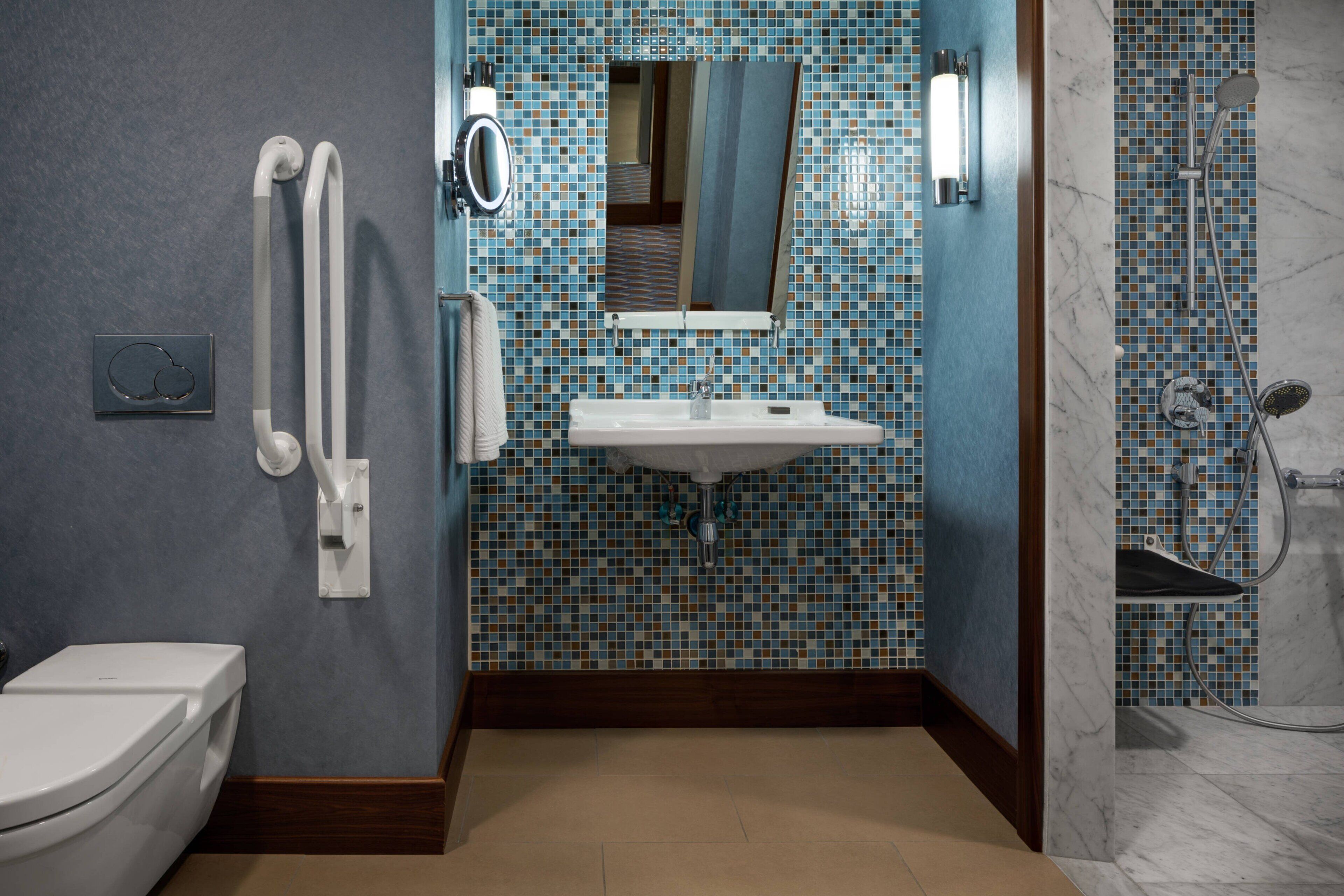 Un bagno con il water bianco, un lavandino con uno specchio sopra e una doccia con pareti in piastrelle.