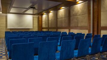 A conference room with rows of blue chairs, a large screen, and a patterned carpet.