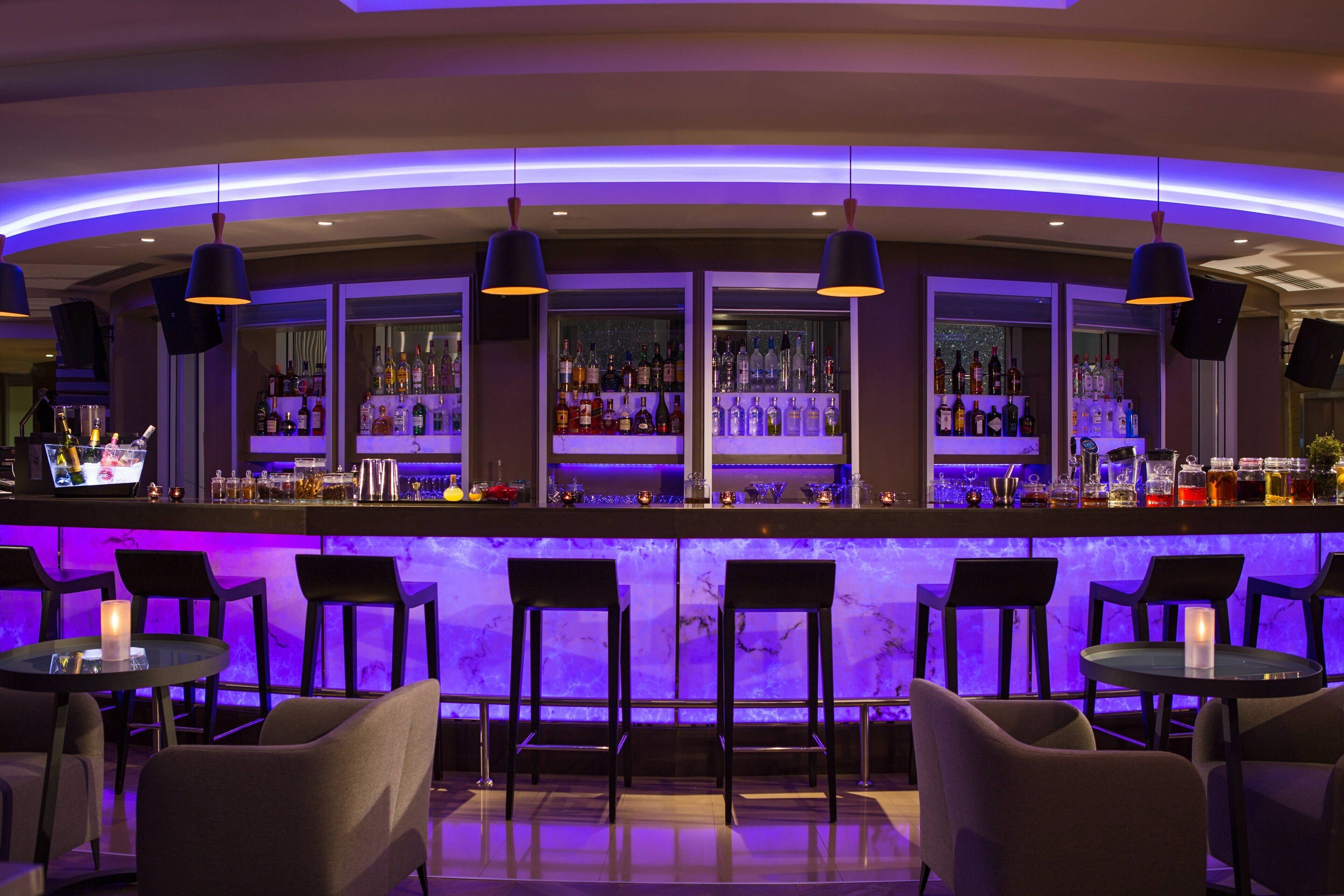 A bar area with a curved counter, multiple shelves of bottles, and bar stools.