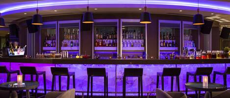 Zona de bar con una barra curva, estantes con varias botellas y taburetes.