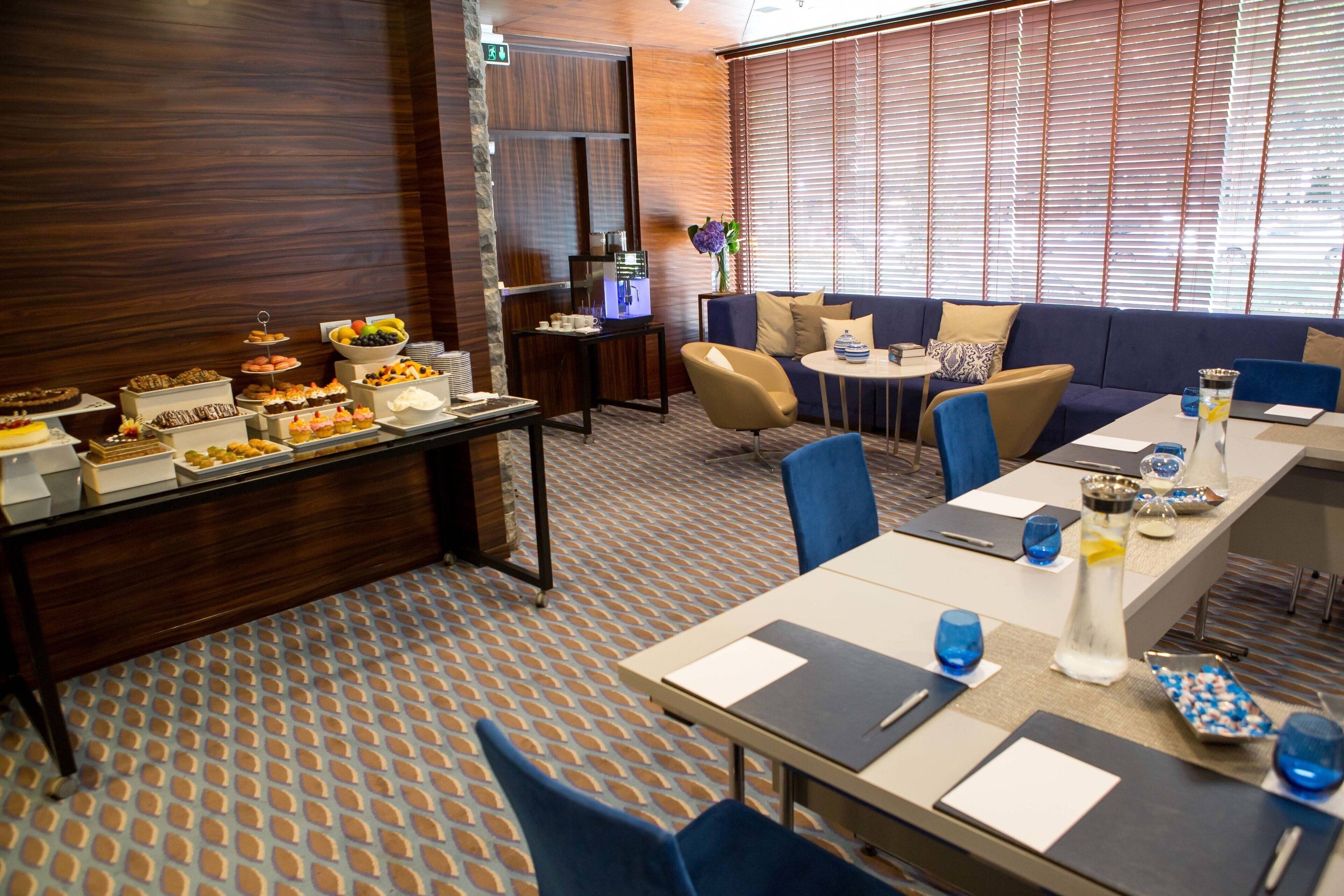 Ein Hotelzimmer mit Essbereich, der ein Buffet mit verschiedenen Desserts und eine Sitzecke mit Sofa und Stühlen bietet.