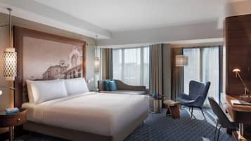 A hotel room with a large bed, a desk, a chair, and a sofa.