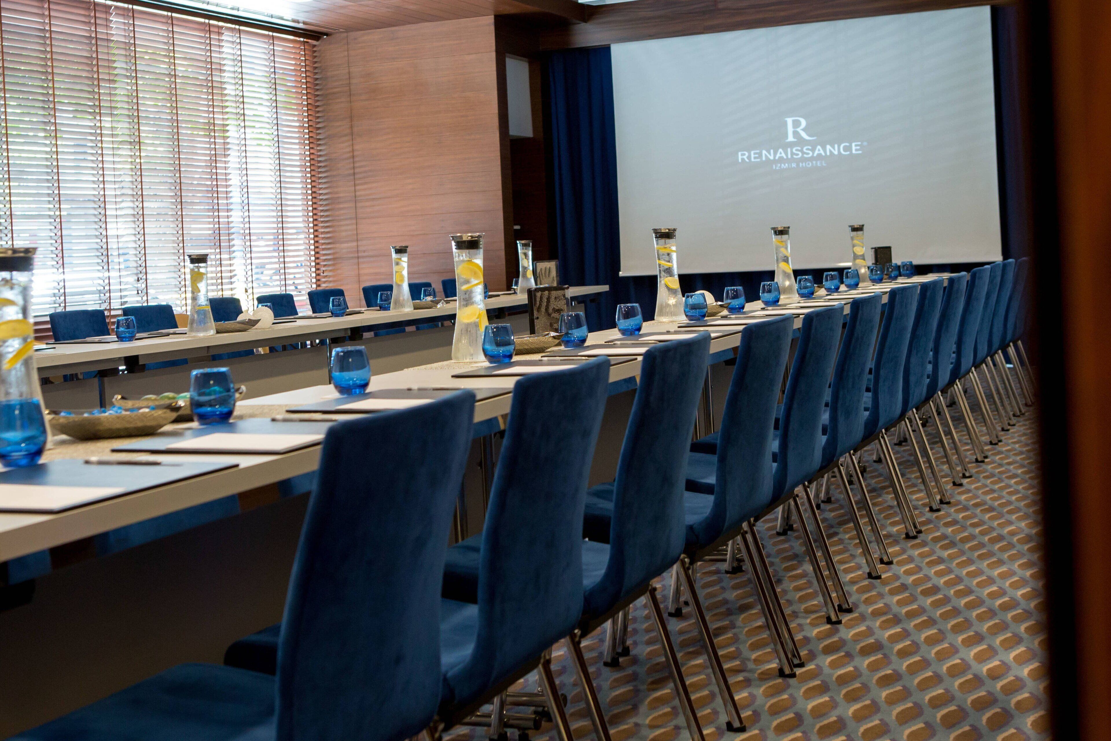 Un salón de conferencias con una mesa larga, sillas azules y una pantalla que muestra el nombre del hotel RENAISSANCE.